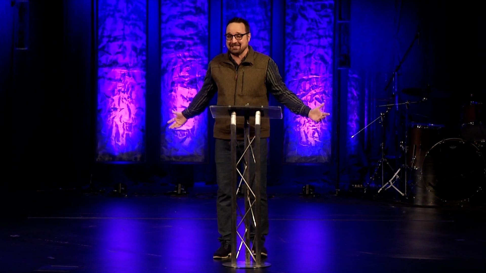 Man preaching with purple lights behind him.