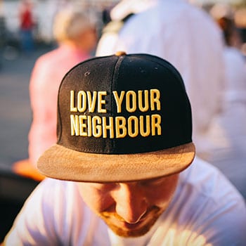 Love your neighbour is written on a baseball cap that a guy wears.