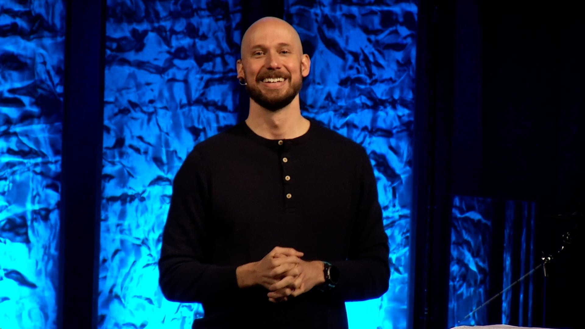 Man preaching on stage with blue lights behind him.