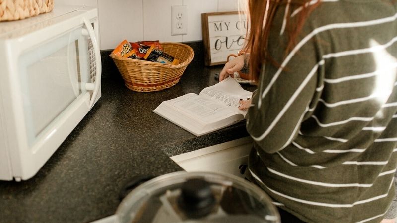 woman reading book at a kitchen counter.