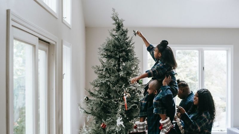 Family hoisting a child in the air to put a star on a tree.